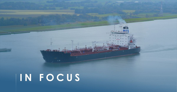 Tanker with a dark hull and white aft superstructure under way on a river past green fields