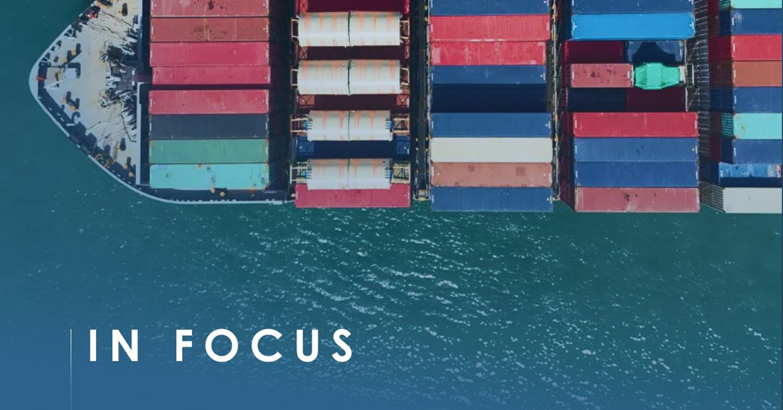 Aerial top-down view of a container ship's bow at sea, deck stacked with red, blue and teal containers