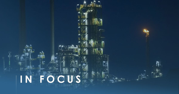 Lit refinery distillation column and burning flare stack against a deep blue dusk sky