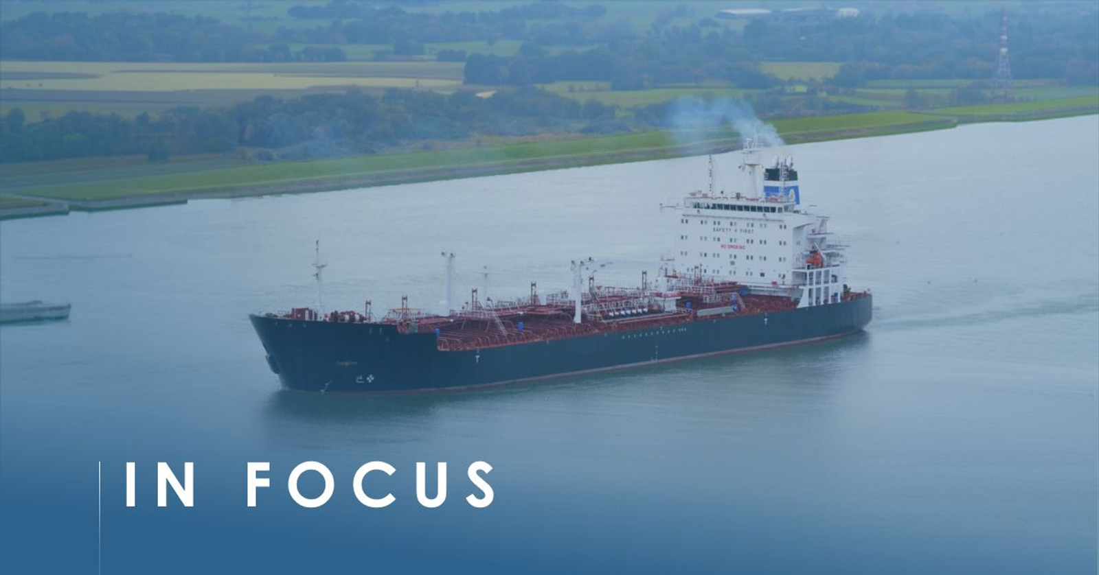 Medium-range product tanker under way on a canal past green fields, captioned In Focus