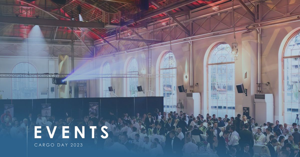Full banquet tables in a hall with arched windows and steel roof trusses, caption CARGO DAY 2023