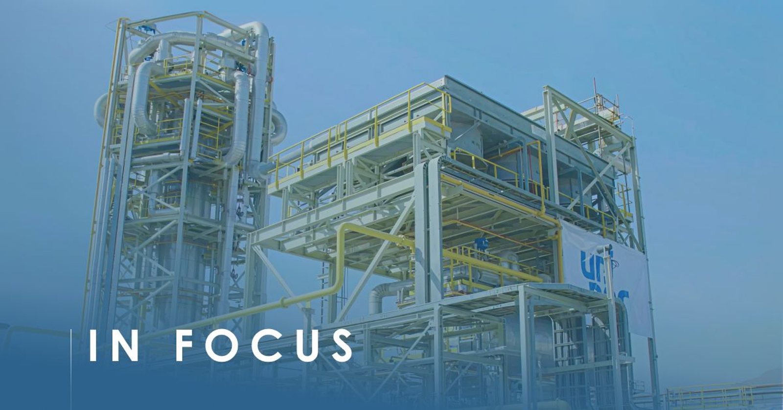 Crude oil processing unit of steel columns and yellow pipework against a pale sky, white banner hung on it