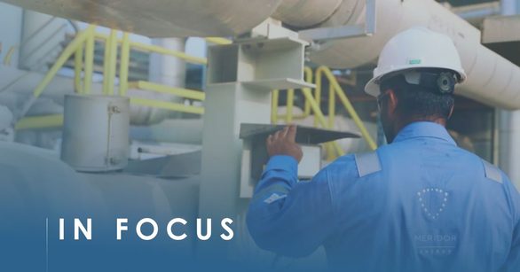 Worker in a white hard hat and blue coveralls with a MERIDOR logo checking plant pipework